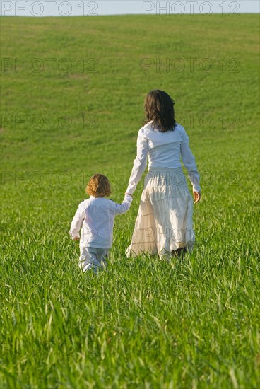 Mother and son holding hands in field rear view