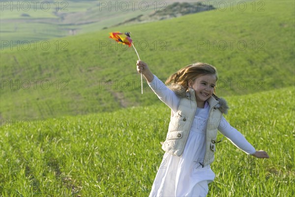 young girl with wind wheel running in green fields