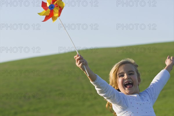 young girl with wind wheel running in green fields
