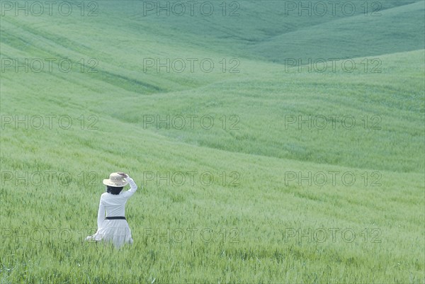 Woman in white dress walking through rolling hills of young wheat