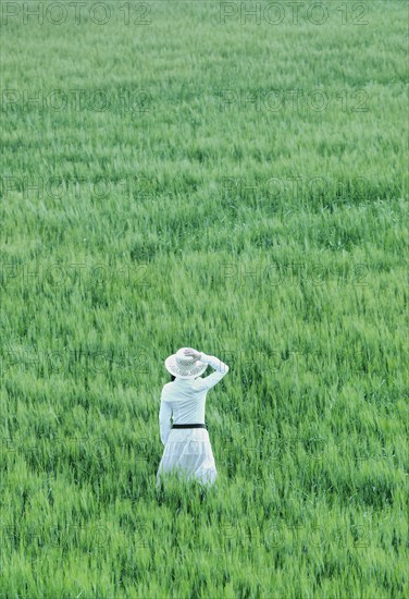 Woman wearing hat standing in field rear view