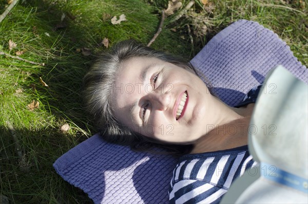 woman lying in grass on picnic rug holding book