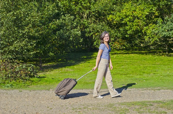 woman walking though park pulling roller case
