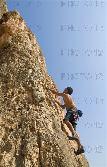 Male free climber scaling rock face low angle view