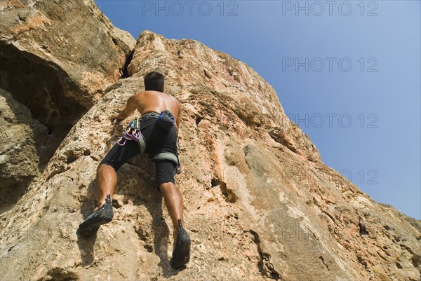 Male free climber scaling rock face rear view low angle view