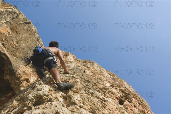 Male free climber scaling rock face rear view upward view
