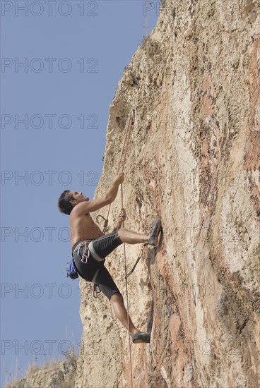 Male rock climber scaling rock face secured by ropes low angle view