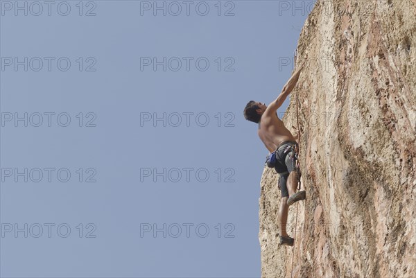 Male rock climber scaling rock face secured by ropes low angle view