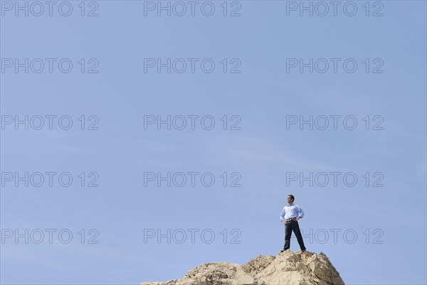 Businessman standing on top of rock looking into distance