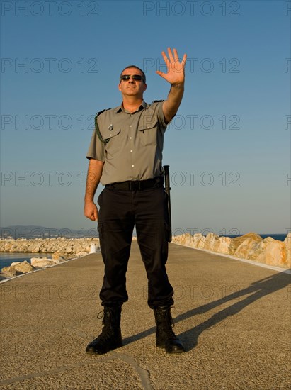 Security guard standing on concrete pier with hand raised