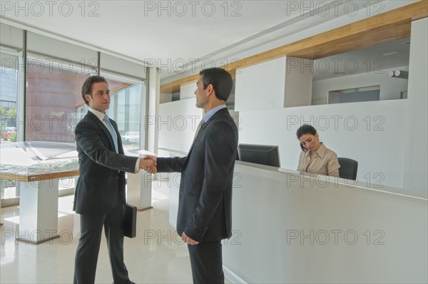 two businessmen shaking hands in office reception