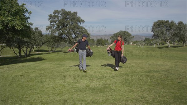 Caucasian couple carrying golf bags on course
