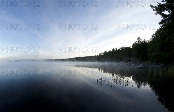 Mist clouds over still lake in remote landscape