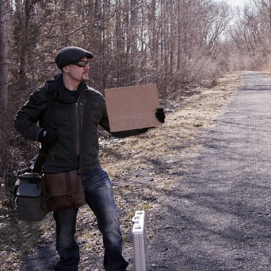 Man hitchhiking with blank sign on rural road