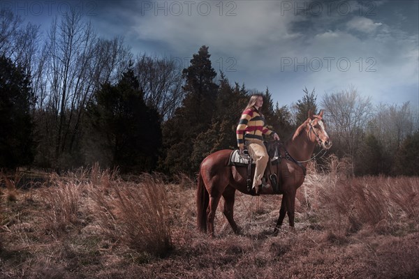 Caucasian woman riding horse in rural field