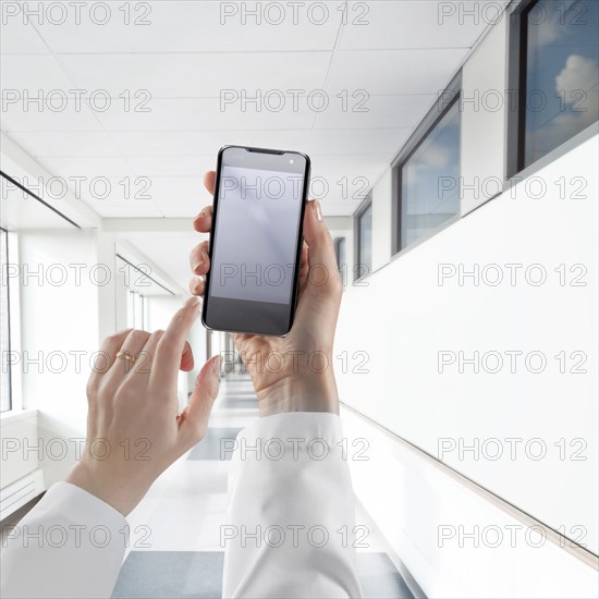 Businesswoman using cell phone in white corridor
