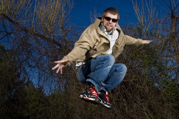 Man wearing sunglasses jumping for joy in forest