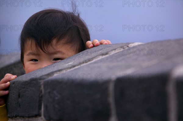 Eyes of boy peeking over stone wall