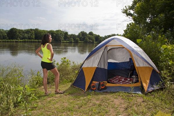 Hispanic woman standing near camping tent at lake