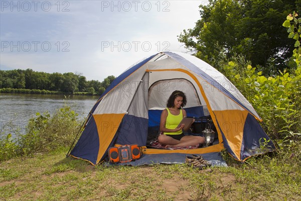 Hispanic woman using digital tablet in camping tent at lake