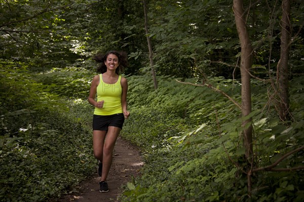 Hispanic woman running on path in forest
