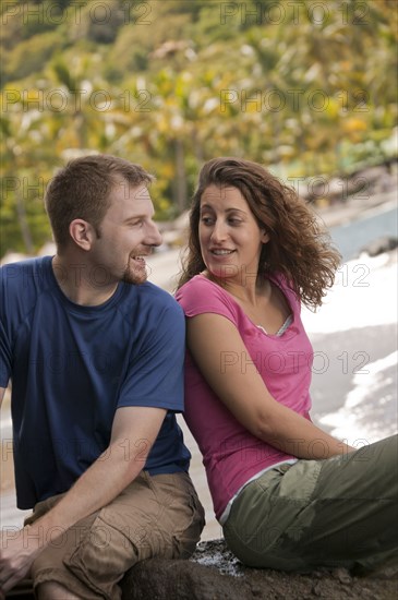 Caucasian couple sitting on rock at beach