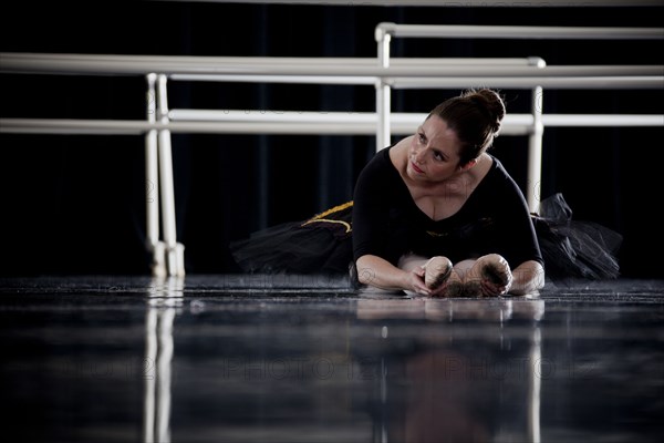 Caucasian ballerina stretching legs on dark stage