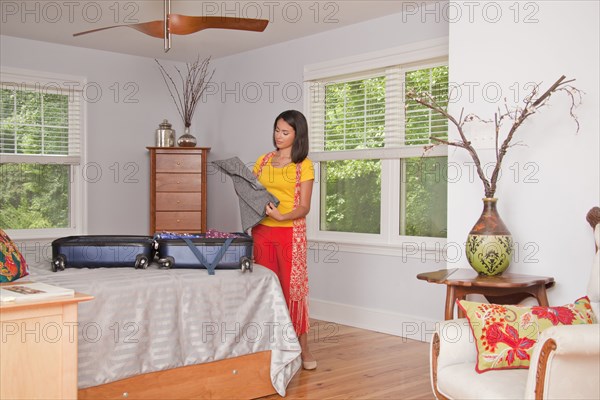 Hispanic woman packing suitcase in bedroom
