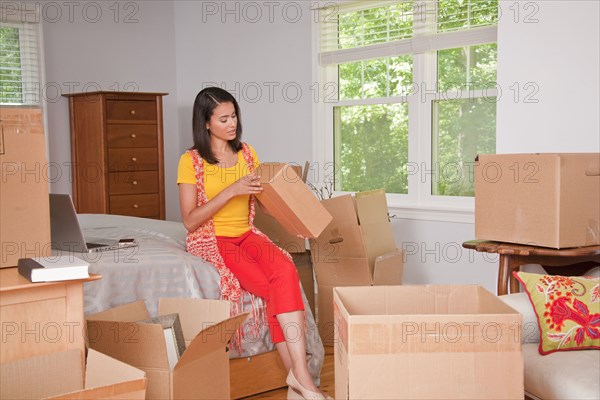 Hispanic woman examining cardboard box in bedroom