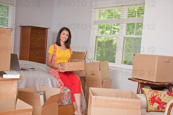 Smiling Hispanic woman holding cardboard box in bedroom