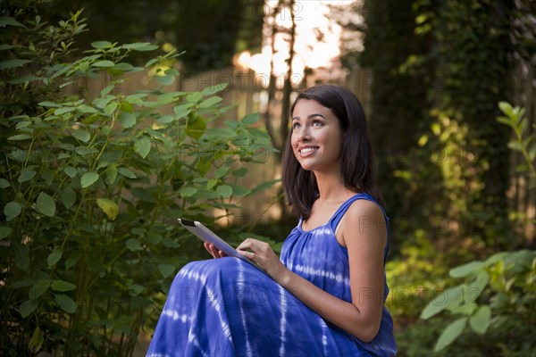 Smiling Hispanic woman using digital tablet in backyard