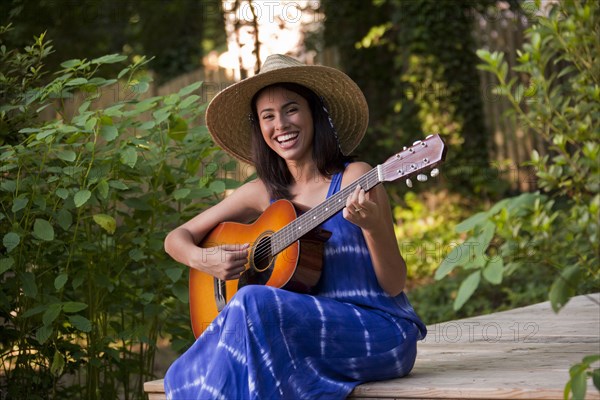 Laughing Hispanic woman playing guitar on patio in backyard