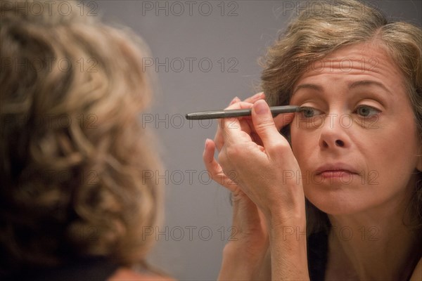 Caucasian woman applying eyeliner in mirror