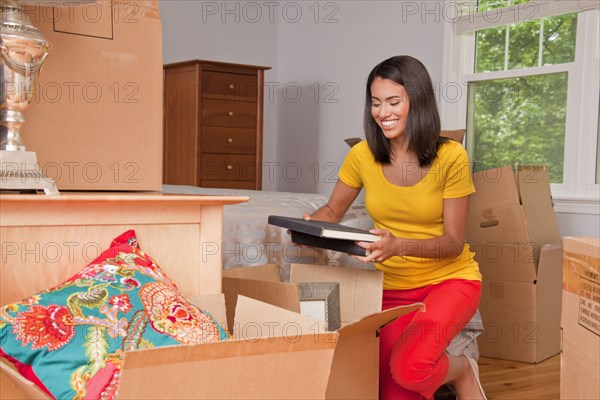 Hispanic woman kneeling on floor packing books in moving boxes