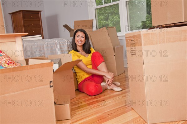 Smiling Hispanic woman sitting on floor with moving boxes