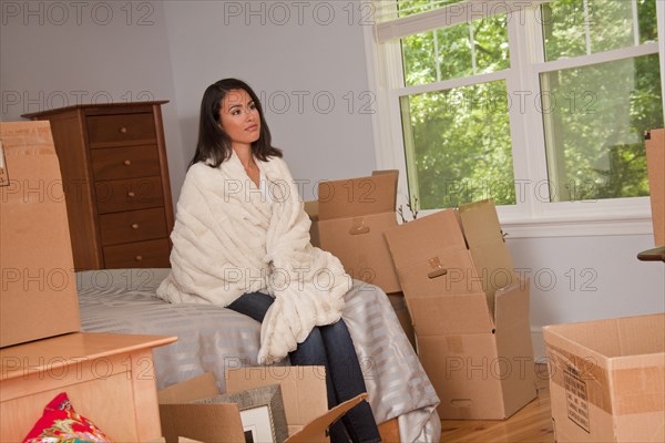 Pensive Hispanic woman sitting on bed near moving boxes