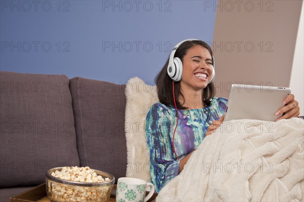 Laughing Hispanic woman sitting on sofa with digital tablet