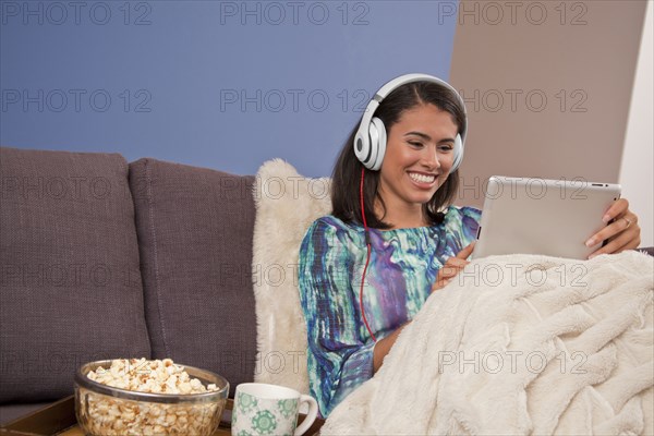 Smiling Hispanic woman sitting on sofa with digital tablet