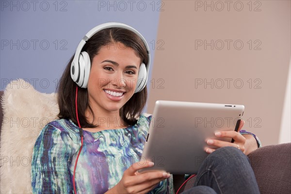 Smiling Hispanic woman sitting on sofa with digital tablet