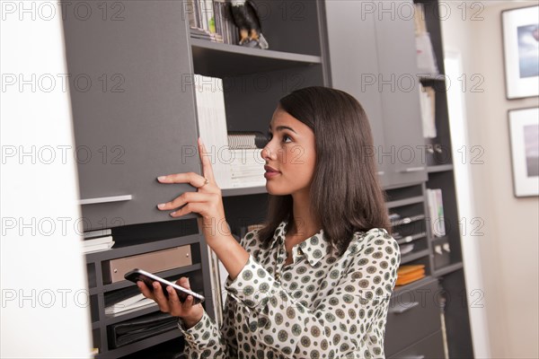 Hispanic businesswoman holding cell phone opening office cabinet