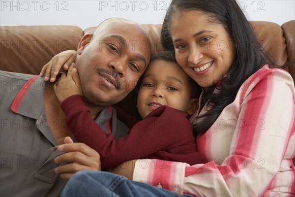 Mixed race boy snuggling on couch with parents