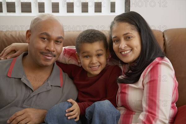 Mixed race boy snuggling on couch with parents