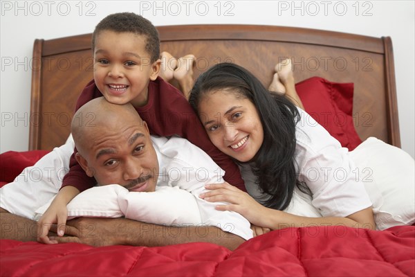 Mixed race boy lounging on bed with parents