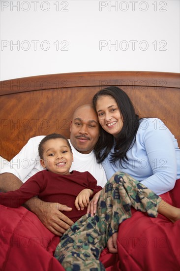 Mixed race boy lounging in bed with parents