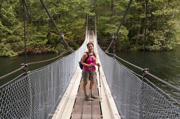 Hispanic woman hiking over bridge in woods