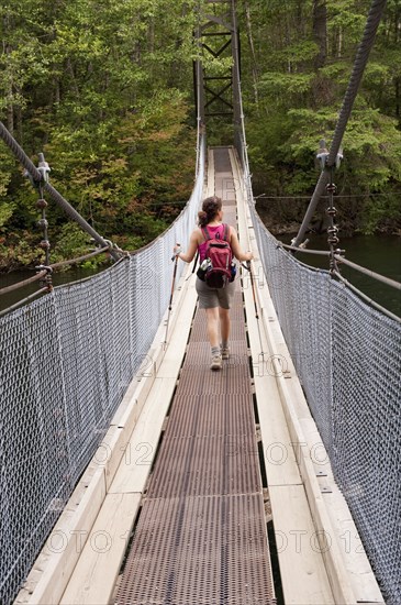 Hispanic woman hiking over bridge in woods