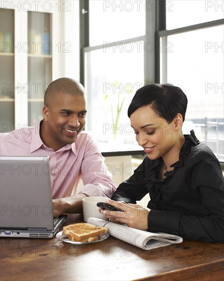 Couple eating breakfast and using laptop and cell phone