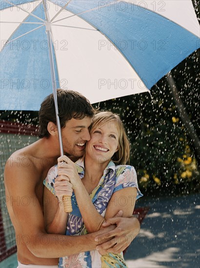 Caucasian couple hugging under umbrella