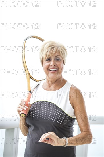 Older Caucasian woman holding tennis racket on balcony