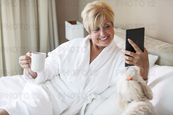 Older Caucasian woman and dog using digital tablet on bed